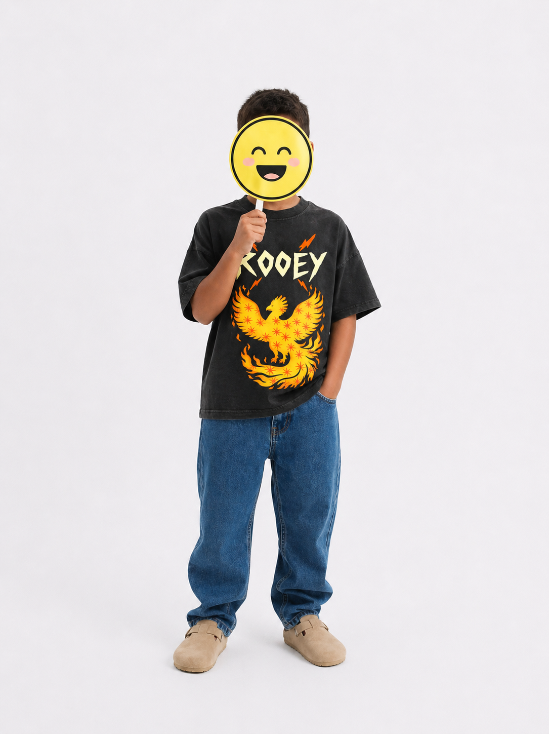 Person wearing a black t-shirt with a phoenix design and text, holding a yellow smiley face mask.