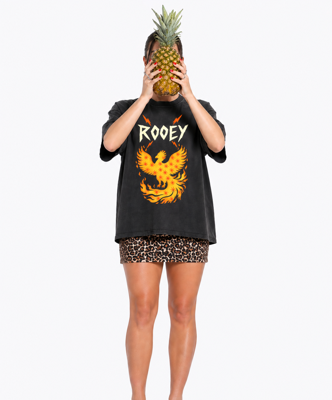 Person wearing a black oversized t-shirt with a phoenix design and 'Rooey' branding, holding a pineapple.